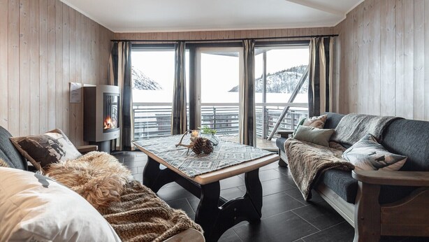 A cozy room with a fireplace, a sofa, a table, and large windows overlooking a snowy landscape. - Hemsedal apartment with 3 bedrooms, 2 bathrooms and sauna (Buskerud)