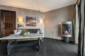 A cozy room with a wooden wall panel, a fireplace, a sofa with cushions, and a table with decorative items. - Hemsedal apartment with 3 bedrooms, 2 bathrooms and sauna (Buskerud)