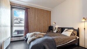 A bedroom with a bed, a window with curtains, a nightstand, and a wall-mounted lamp. - Hemsedal apartment with 3 bedrooms, 2 bathrooms and sauna (Buskerud)