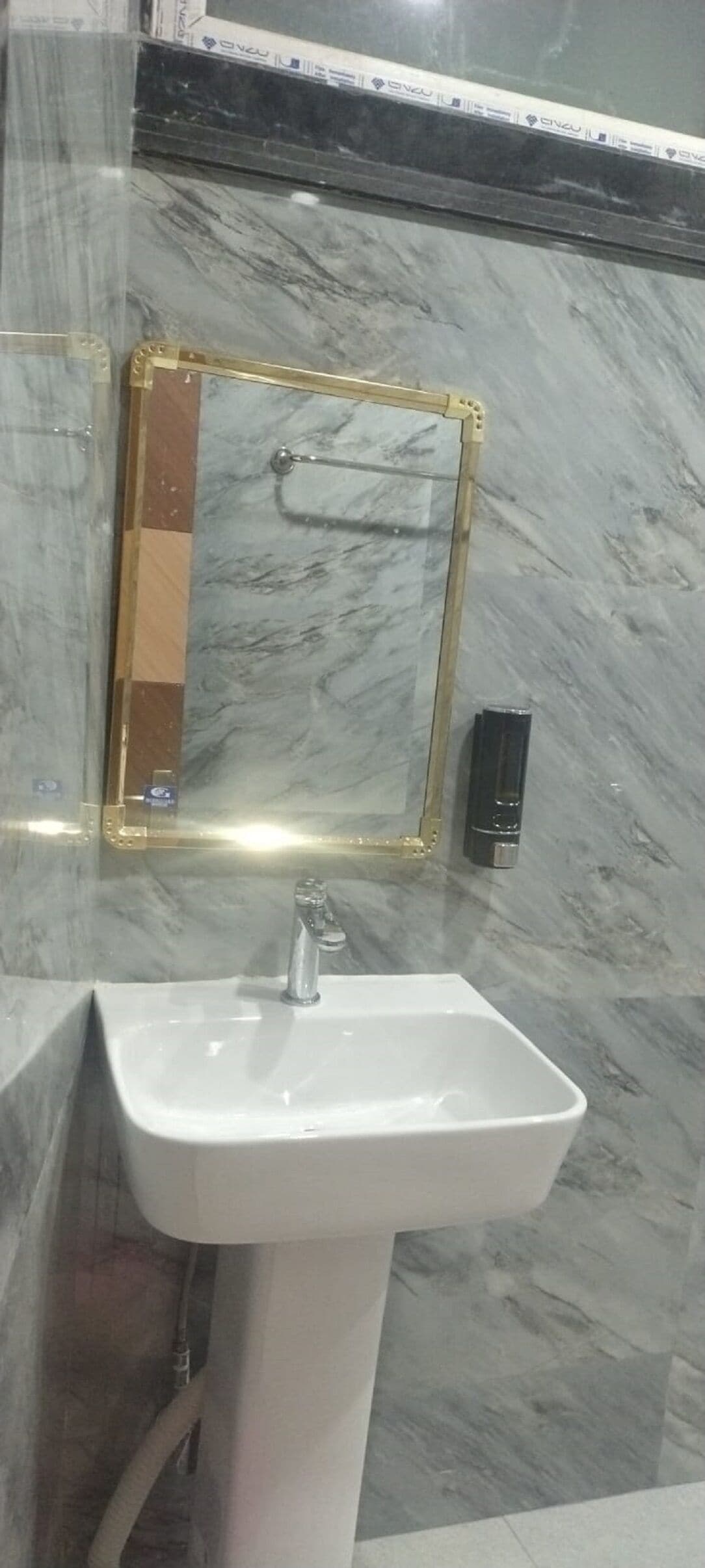 Ένα μπάνιο με έναν λευκό νιπτήρα, έναν καθρέφτη με χρυσό πλαίσιο και έναν μαύρο διανομέα σαπουνι ού.