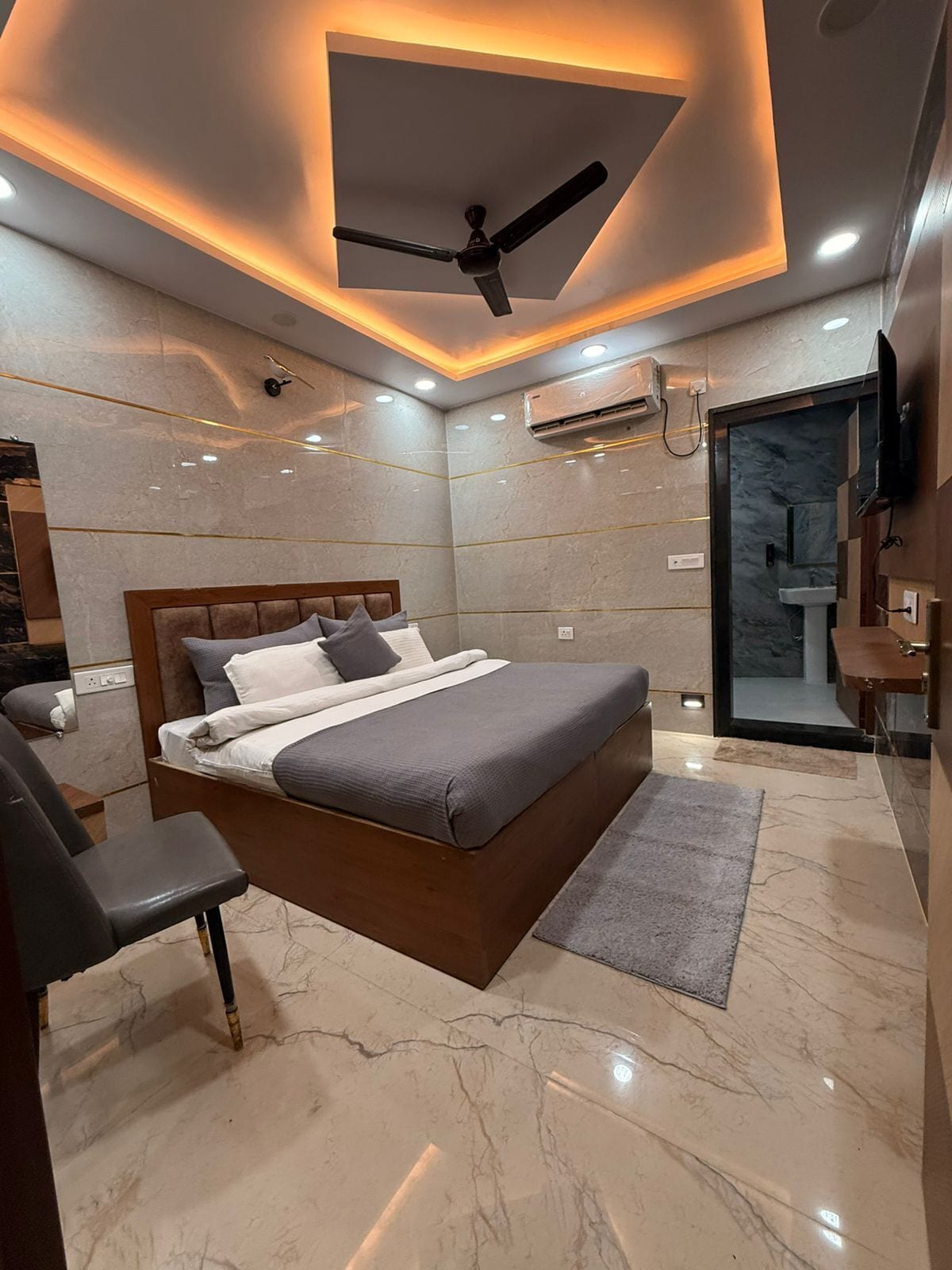 Une chambre à coucher moderne, équipée d’un lit, d’un ventilateur de plafond, d’un appareil de climatisation et d’une salle de bain avec un lavabo.