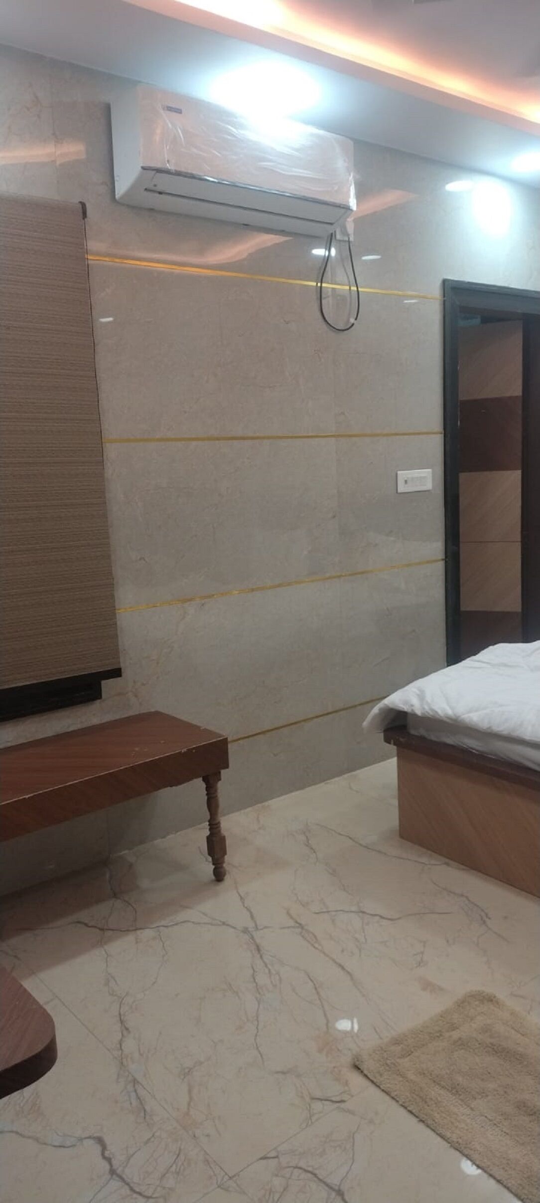 A room with a bed, a bench, a wall-mounted air conditioner, and a tiled floor.