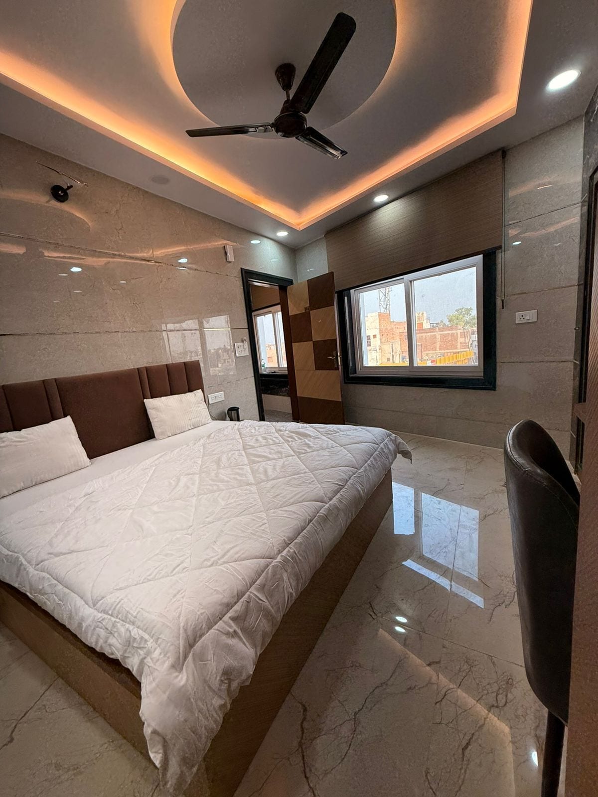A bedroom with a large bed, a ceiling fan, a window with a view, and a marble floor.