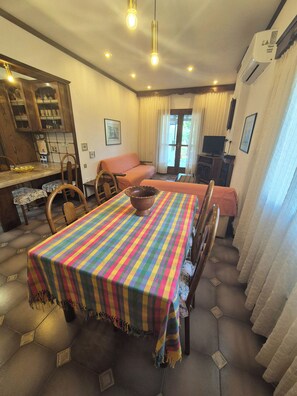 A dining area with a striped tablecloth, wooden chairs, a sofa, and a television. - GeoVilla 2 - Pefkochori Glarokavos (Pefkochori)