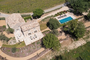 Vue aérienne d’une villa dotée d’une piscine, entourée de jardins aménagés et d’un vignoble.