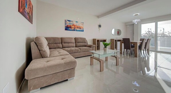 Ein modernes Wohnzimmer mit einem Ecksofa, einem Glastisch und einem Essbereich mit Stühlen und einem Tisch.