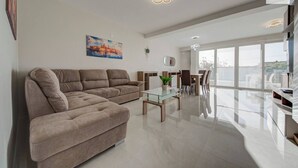 Uma sala de estar moderna com sofá seccional, mesa de centro de vidro e área de jantar com cadeiras. Há um quadro na parede e uma placa indicando '360 Estates'.