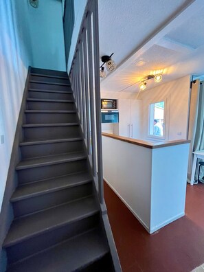 A staircase leading to a kitchen area with a microwave and cabinets. - Maison Piranga by Agence Bru - 731672 (Lacanau)