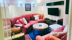 Una sala de estar con un sofá rojo, una mesa de centro redonda, un televisor de pantalla plana y un tablero de ajedrez.