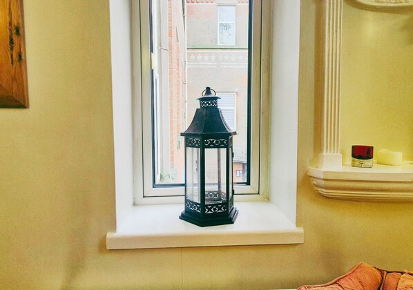A black lantern on a white window sill with a view of a brick building outside.
