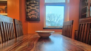 Una mesa de comedor con un bol en el centro, rodeada por sillas de madera, en una habitación con paredes anaranjadas y una ventana.