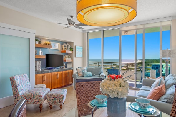 A living room with a television, wicker furniture, and a view of the ocean. - Ocean Club. Gulf Views. Pool. Walk to Beach (Biloxi)