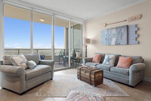 A living room with two sofas, a coffee table, and a view through a sliding glass door to a balcony. - Ocean Club. Gulf Views. Pool. Walk to Beach (Biloxi)