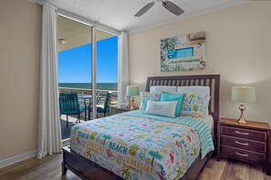 A bedroom with a large bed, a balcony with a view of the ocean, and a ceiling fan. - Ocean Club. Gulf Views. Pool. Walk to Beach (Biloxi)