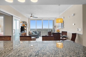A modern kitchen with granite countertops, a dining area with wicker chairs, and a large window offering a view of the sky. - Ocean Club. Gulf Views. Pool. Walk to Beach (Biloxi)