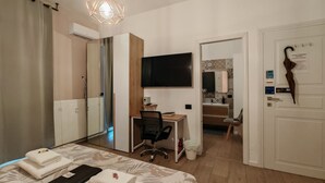 Hotellihuone, jossa on sänky, työpöytä, tuoli, televisio, peilillä varustettu kylpyhuone ja ovi, jossa on sateenvarjo.