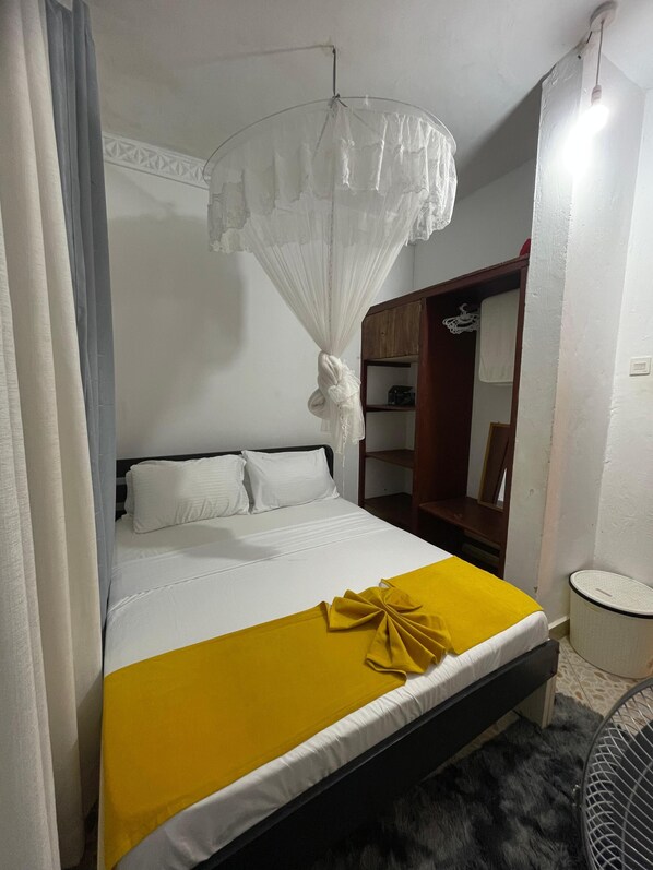 Una cama con una colcha blanca y amarilla, un dosel blanco y un armario de madera.