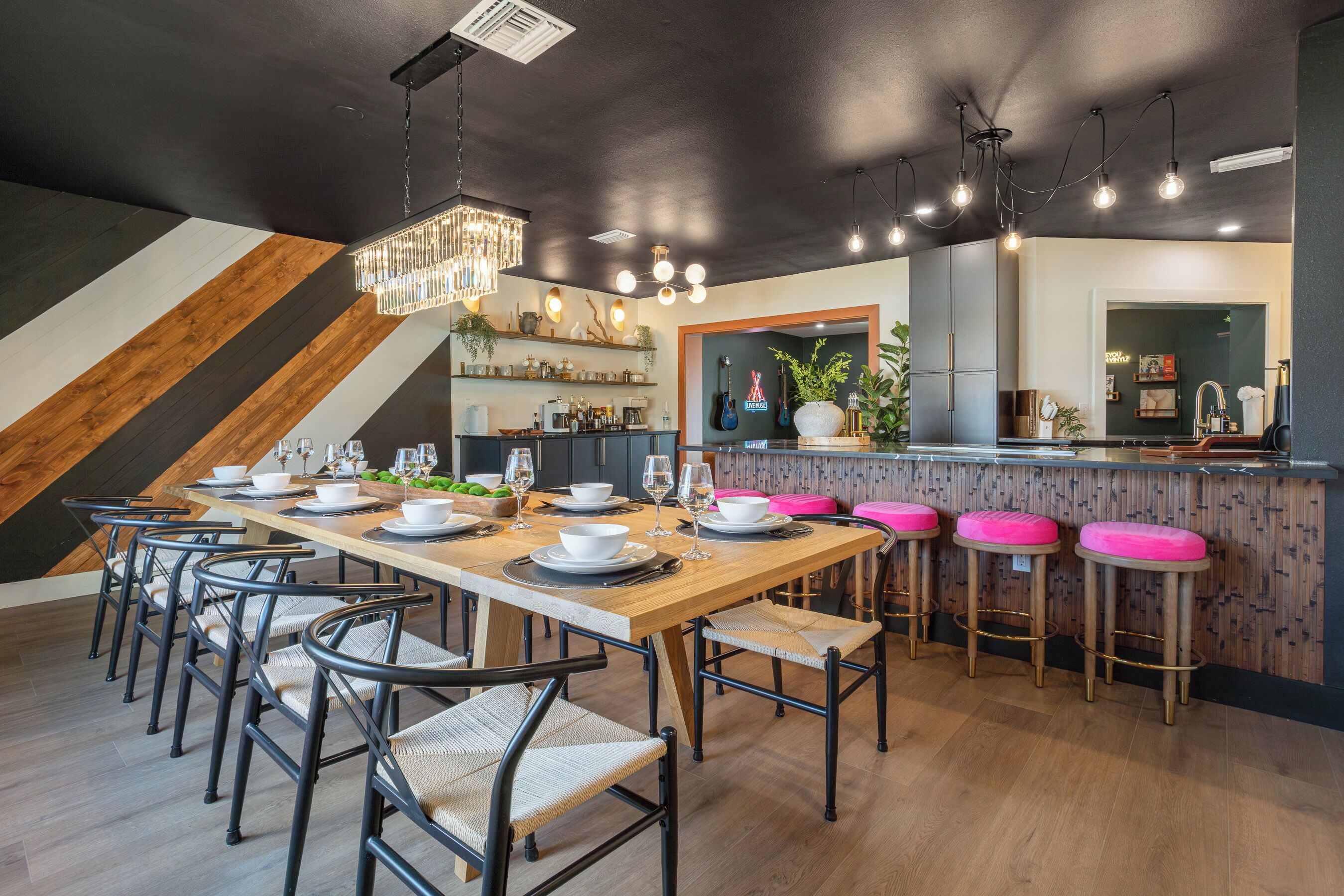 A modern kitchen with a wooden bar area, bar stools, and a dining table set for six.