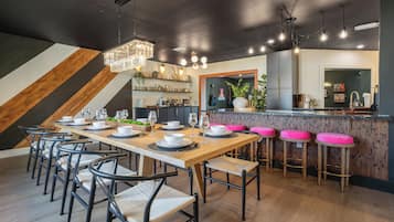 A modern kitchen with a wooden bar area, bar stools, and a dining table set for six.