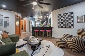 Una sala de estar moderna con un sofá, una mesa de centro, un tapete estampado, un ventilador de techo y una zona de bar con taburetes.
