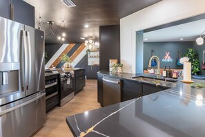 A modern kitchen with stainless steel appliances, a black marble countertop, and a unique wooden accent wall. - 5BR Pool & Game Room Retreat • Near Gulf Beaches (Seminole)