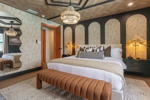 Un dormitorio con una cama grande, un banco de madera, un espejo y una araña.