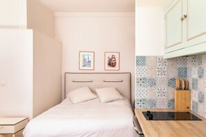 Ein Schlafzimmer mit einem Bett, einem Nachttisch, einer Wandregal und einer Küchenzeile mit gefliestem Fliesenspiegel und einem Holzkorpus.