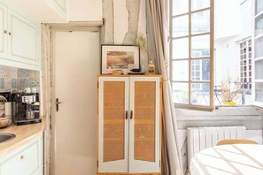 A room with a kitchenette, a rattan cabinet, a window with curtains, and a radiator. - Cozy Bright Studio for 2 Saint Germain des Pres (Paris)