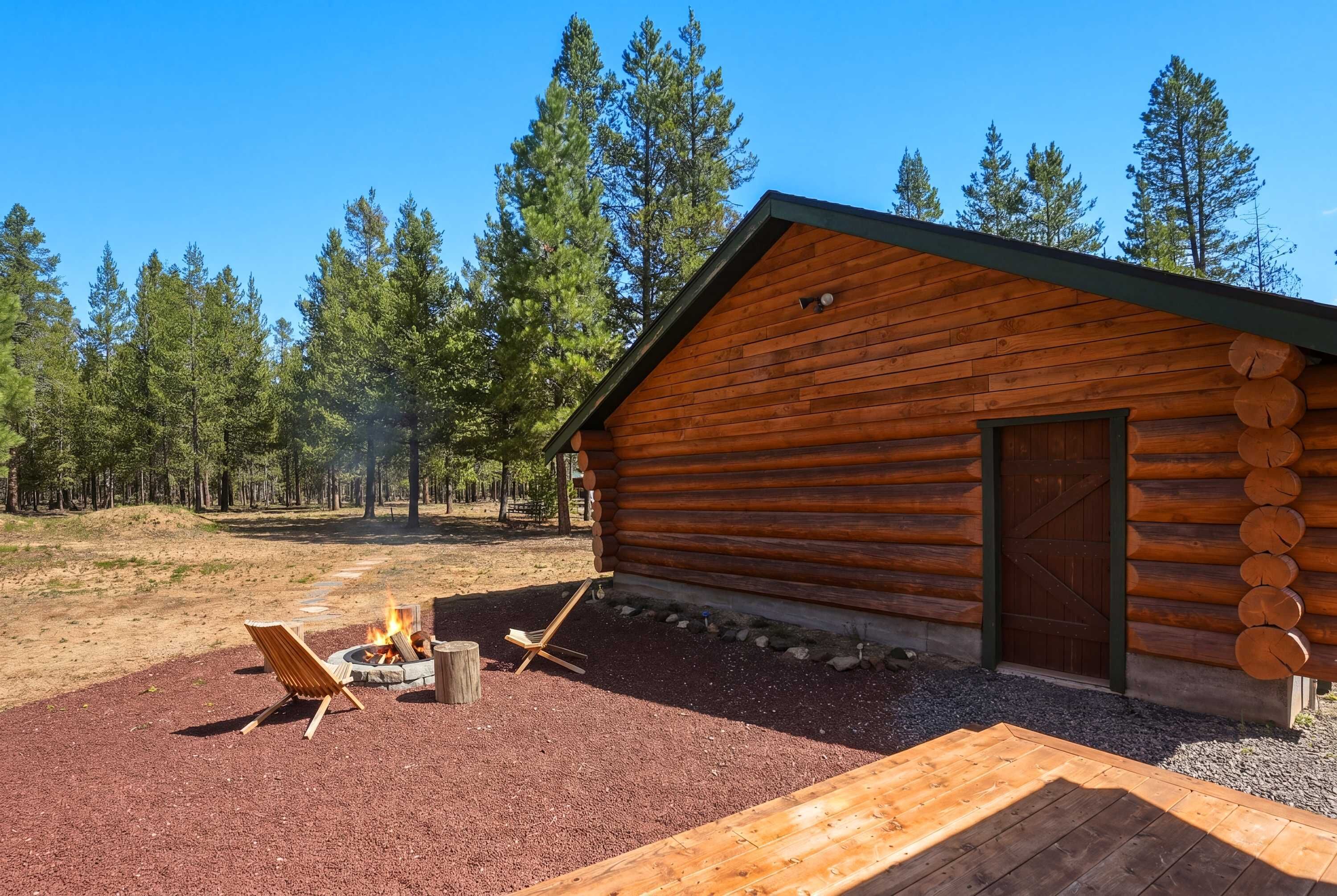 A log cabin with a fire pit and a bench outside.