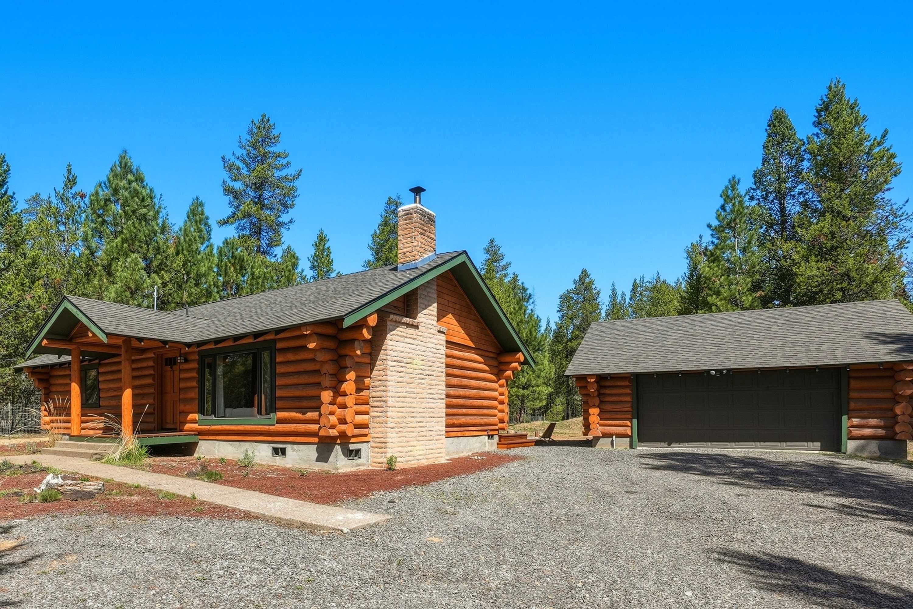 A log cabin with a chimney, a garage, and a gravel driveway.