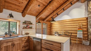 Ein Interieur einer Blockhütte mit Holzschränken, einer weißen Arbeitsplatte, einem eingebauten Geschirrspüler und einer Steinwand.