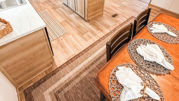 A modern kitchen with wooden cabinets, a central island, and a dining area with a table set for two. - Emily’s Beach Shack at Holden Beach! Charming NEW home about 1 mile from beach! (Supply)