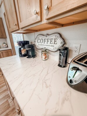 A kitchen with marble countertops, a coffee sign, a coffee maker, a toaster, and wooden cabinets.