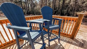 A deck with two blue Adirondack chairs and a small table. - Emily’s Beach Shack at Holden Beach! Charming NEW home about 1 mile from beach! (Supply)