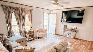 A living room with a sofa, armchairs, a TV, and a ceiling fan. - Emily’s Beach Shack at Holden Beach! Charming NEW home about 1 mile from beach! (Supply)