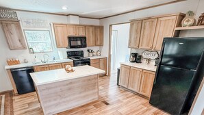 A modern kitchen with wooden cabinets, a black refrigerator, and a central island. - Emily’s Beach Shack at Holden Beach! Charming NEW home about 1 mile from beach! (Supply)