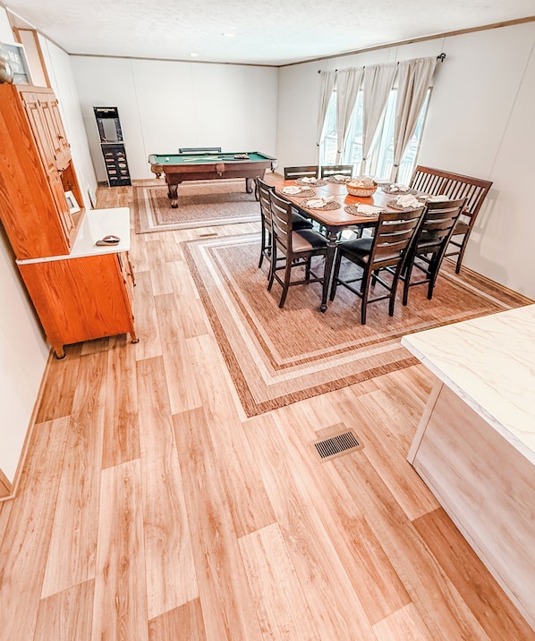 A dining area with a pool table, wooden chairs, and a white table.