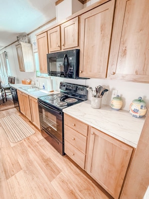 A kitchen with wooden cabinets, a black microwave, a stove, and a marble countertop.
