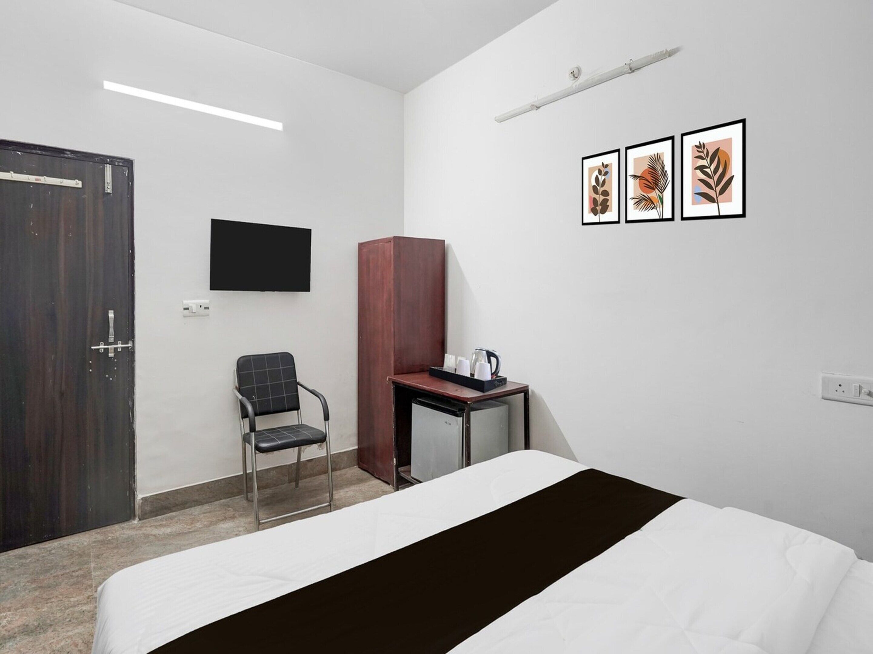A hotel room with a bed, a desk with a coffee maker, a chair, a TV mounted on the wall, and framed artwork.