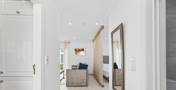 A hallway leading to a bedroom with a bed, a bedside table, a chair, and a large mirror. - The Studio - VALE DO LOBO (Vale do Lobo)