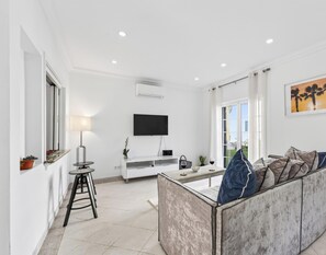 A modern living room with a flat-screen TV, a sofa, a coffee table, and a dining area with a table and chairs. - The Studio - VALE DO LOBO (Vale do Lobo)