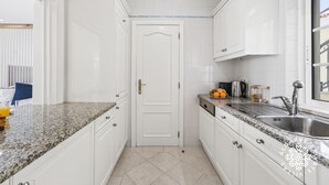 Una cucina con mobili bianchi, piani di lavoro in granito, un lavello in acciaio inossidabile e una porta con maniglia.