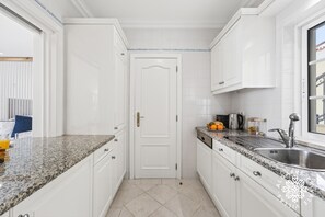 A kitchen with white cabinets, granite countertops, a stainless steel sink, and a door with a handle. - The Studio - VALE DO LOBO (Vale do Lobo)