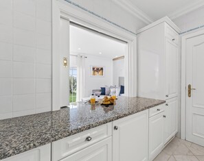 A kitchen with white cabinets, granite countertops, and a view into the dining area. - The Studio - VALE DO LOBO (Vale do Lobo)