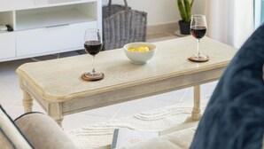 Un soggiorno con un tavolino in legno, due bicchieri da vino, una ciotola di burro, un mobiletto bianco e una pianta in vaso.