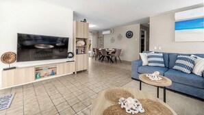Uma sala de estar com televisão, sofá, mesa de jantar e cadeiras.