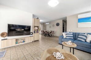 Ein Wohnzimmer mit Fernseher, Sofa, Esstisch und Stühlen.