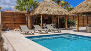 Área de piscina com espreguiçadeiras e estruturas de telhado de palha.