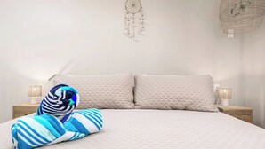Cama bem arrumada com duas almofadas, uma toalha listrada e um sonho apanhador na parede.