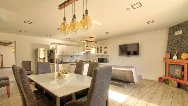A modern dining area with a table and chairs, a kitchen in the background, and a TV mounted on the wall. - Room 'Quarto 2' with Shared Pool, Shared Terrace and Wi-Fi (Moncarapacho)